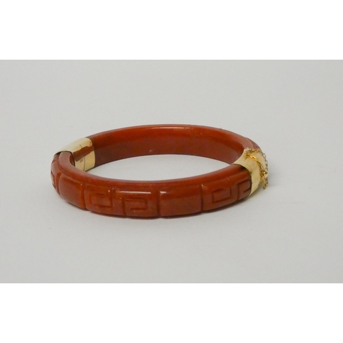 492 - A carved dyed jade hinged bangle with 14ct yellow gold fittings.