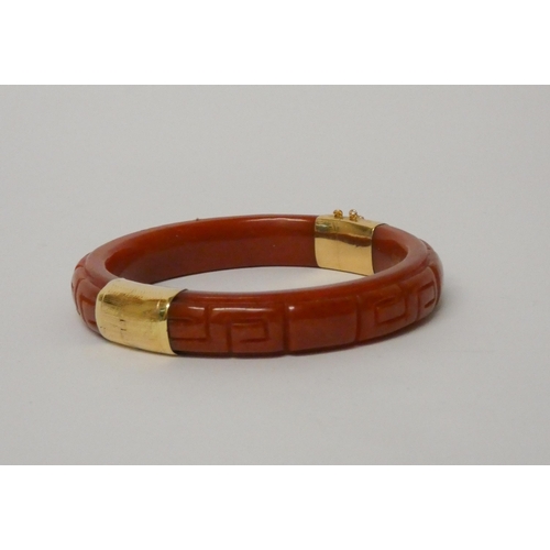 492 - A carved dyed jade hinged bangle with 14ct yellow gold fittings.