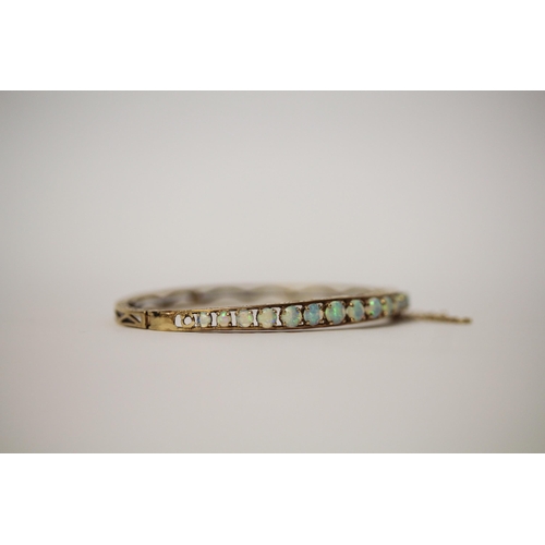 555 - An opal set 9ct gold hinged bangle, with snap clasp and safety chain, hallmarked, gross weight 10g