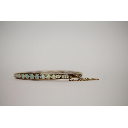 555 - An opal set 9ct gold hinged bangle, with snap clasp and safety chain, hallmarked, gross weight 10g