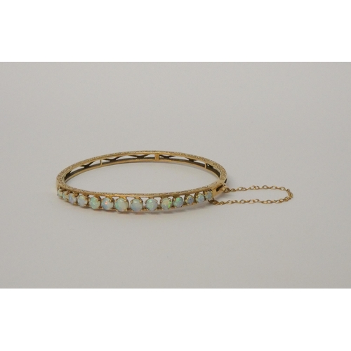 555 - An opal set 9ct gold hinged bangle, with snap clasp and safety chain, hallmarked, gross weight 10g