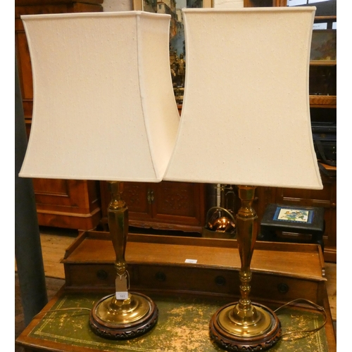 163 - A pair of tall brass candlestick table lamps with cream shades standing on Chinese hardwood bases, 3... 