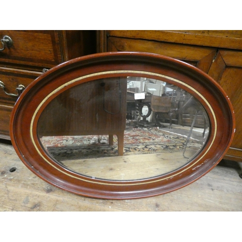 392 - An oval bevelled wall mirror in mahogany and inlaid frame