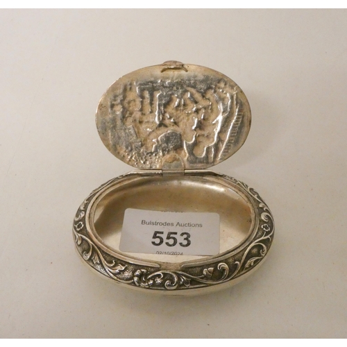 553 - A oval continental silver patch or snuff box, the hinged lid decorated with merry-making scene. Impo... 