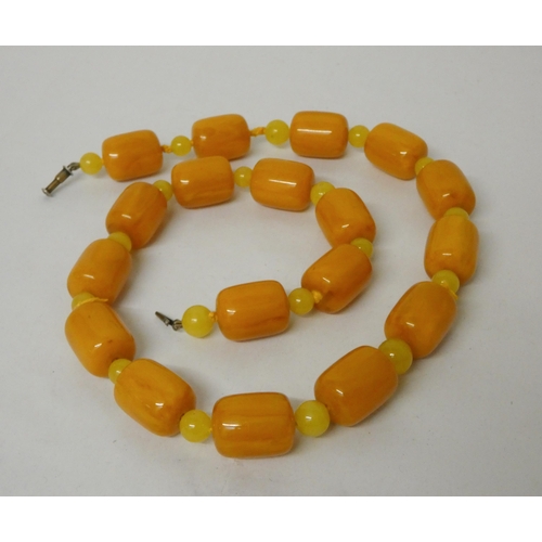 704 - A row of cylindrical butterscotch amber beads, uniform beads measuring approximately 28mm x 20mm eac... 