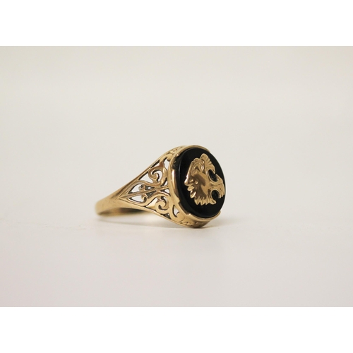 728 - A gents signet ring, the onyx panel with overlaid gold roaring lion motif, on pierced 9ct yellow gol... 