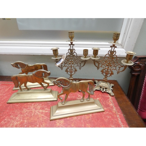 415 - Three brass horse door stops and a pair three branch brass decorative candelabra on paw feet.