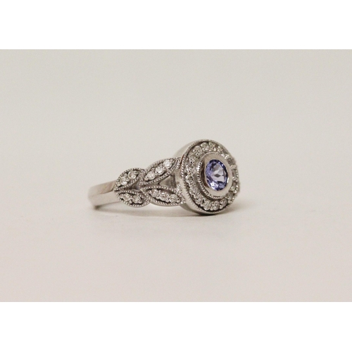 596 - A modern tanzanite and diamond dress ring, the circular tanzanite in 14K white gold collet setting w... 