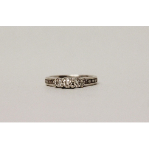 625 - A diamond three stone ring, with channel set diamond shoulders. 14k white gold band. Ring size N, 3.... 