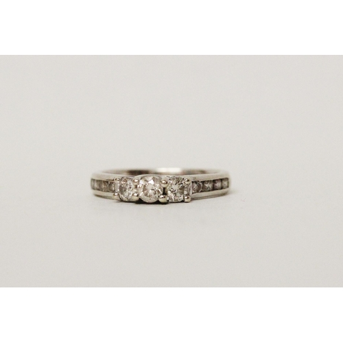 625 - A diamond three stone ring, with channel set diamond shoulders. 14k white gold band. Ring size N, 3.... 