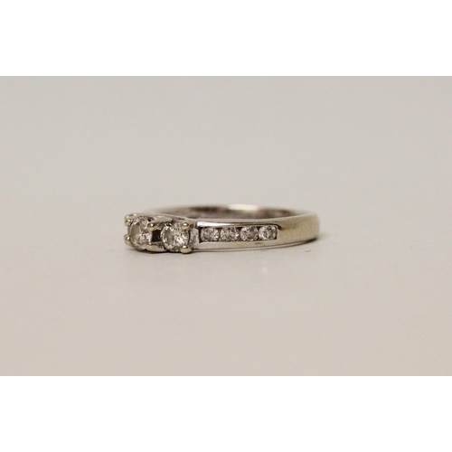 625 - A diamond three stone ring, with channel set diamond shoulders. 14k white gold band. Ring size N, 3.... 