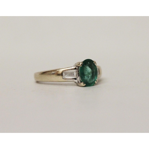 626 - An emerald and diamond ring, the oval claw set emerald flanked by baguette cut diamond shoulders, on... 