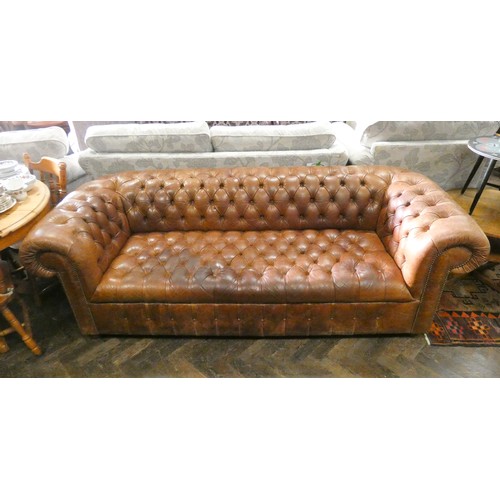 498 - An antiqued brown leather buttoned chesterfield sofa, on turned bun feet.  Approximately 88