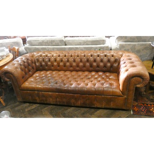 498 - An antiqued brown leather buttoned chesterfield sofa, on turned bun feet.  Approximately 88