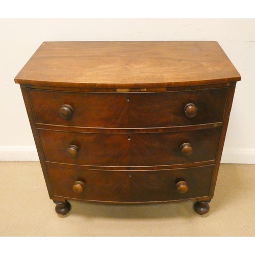 85 - A Victorian mahogany bowfront chest of three long drawers with bun handles standing on turned feet, ... 