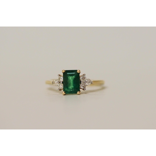 514 - An emerald and diamond ring, the trap cut emerald flanked by brilliant cut diamonds, on yellow metal... 