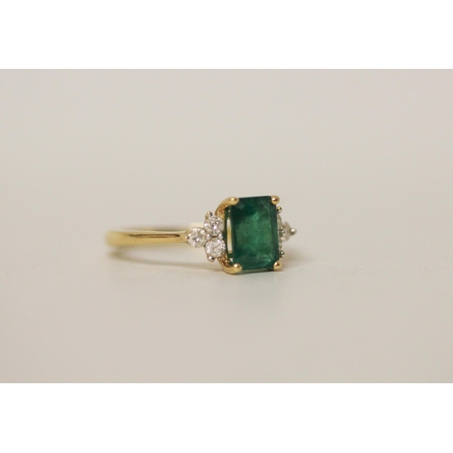 514 - An emerald and diamond ring, the trap cut emerald flanked by brilliant cut diamonds, on yellow metal... 