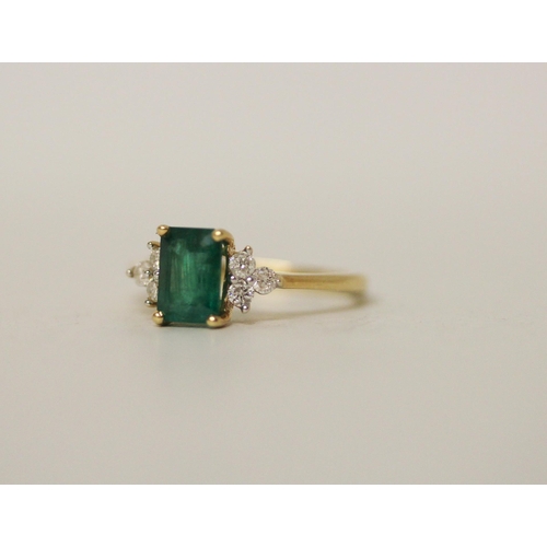 514 - An emerald and diamond ring, the trap cut emerald flanked by brilliant cut diamonds, on yellow metal... 