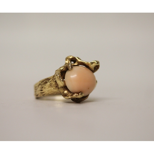 449 - A coral dress ring, the oval angel coral within seaweed inspired naturalistic mount, in unmarked yel... 