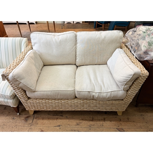 36 - A modern wicker two seater conservatory sofa  with pale beige linen cushions