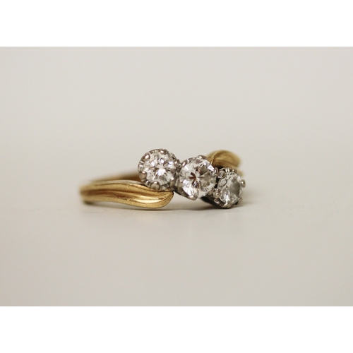 424 - A three stone diamond ring, the three brilliant cut diamonds claw set in a offset cross over twist d... 