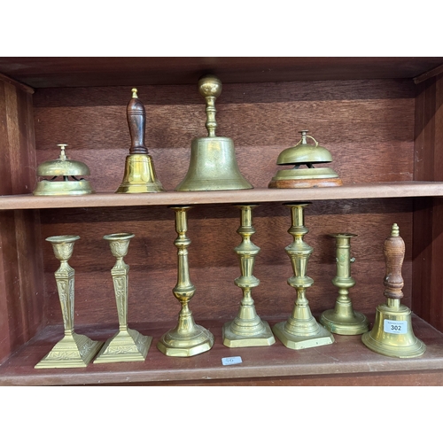 302 - Two pairs of brass candlesticks together with two desk bells, three hand bells and further candlesti... 