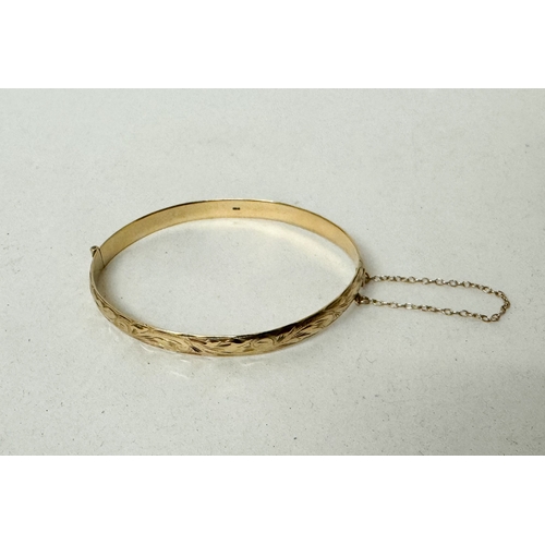 390B - Hallmarked 9ct gold hinged bangle with engraved decoration to one side, safety chain and invisible b... 