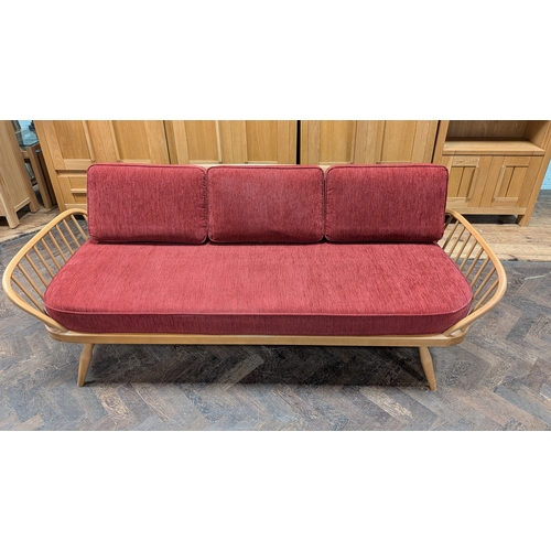 10 - An Ercol blond elm sofa/day bed, model 355, with red cushions...