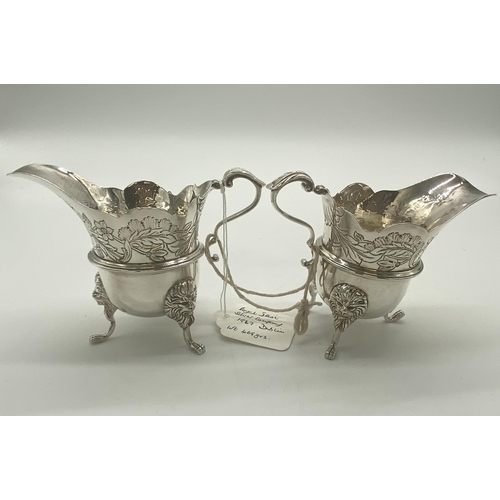 1354 - Pair of Irish silver milk jugs with hand chased florals to the top rim with an open monogram cartouc... 