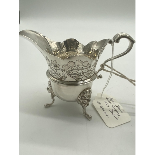 1354 - Pair of Irish silver milk jugs with hand chased florals to the top rim with an open monogram cartouc... 