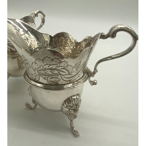 1354 - Pair of Irish silver milk jugs with hand chased florals to the top rim with an open monogram cartouc... 