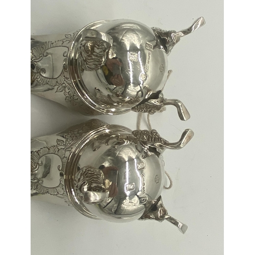 1354 - Pair of Irish silver milk jugs with hand chased florals to the top rim with an open monogram cartouc... 