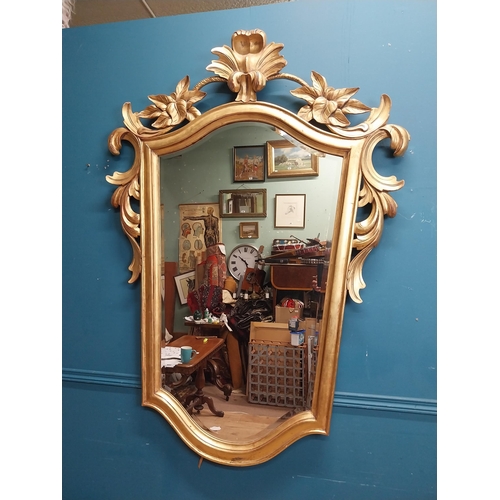 964 - Gilt wall mirror mounted in a shield shaped frame surmounted with foliage. { 157cm H X 110cm W }.