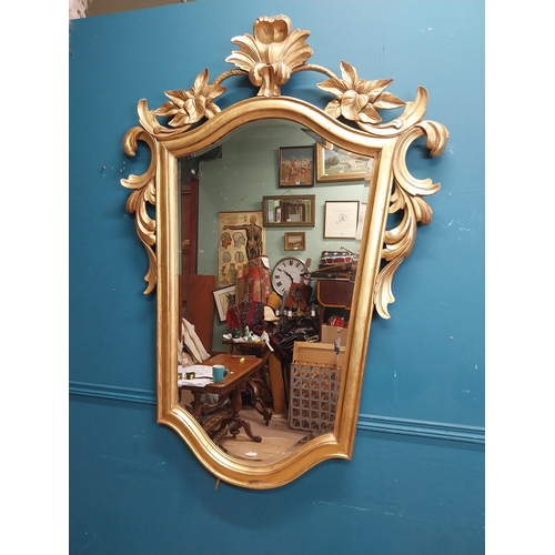 964 - Gilt wall mirror mounted in a shield shaped frame surmounted with foliage. { 157cm H X 110cm W }.