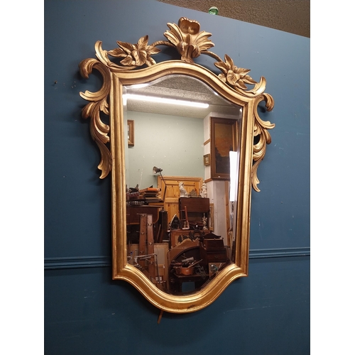 964 - Gilt wall mirror mounted in a shield shaped frame surmounted with foliage. { 157cm H X 110cm W }.