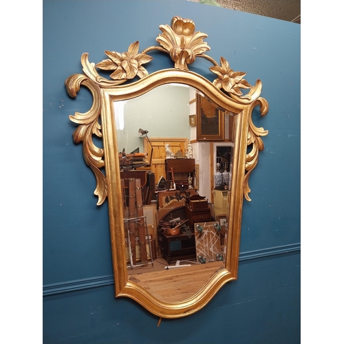 964 - Gilt wall mirror mounted in a shield shaped frame surmounted with foliage. { 157cm H X 110cm W }.