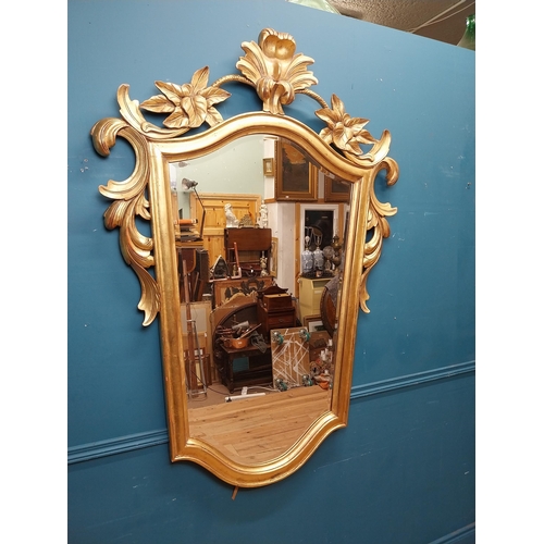 964 - Gilt wall mirror mounted in a shield shaped frame surmounted with foliage. { 157cm H X 110cm W }.