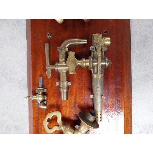 684 - Collection of nine 19th C. brass bar taps mounted on mahogany board. {32 cm H x 82 cm W}.