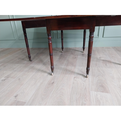 324 - Regency flamed mahogany drop leaf dining table raised on turned legs and brass and ceramic castors {... 