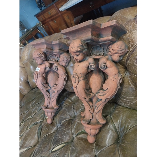 2100 - Pair of moulded terracotta wall brackets decorated with cherubs {53 cm H x 29 cm W x 19 cm D}.