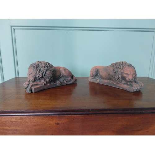 2121 - Pair of moulded terracotta statuettes of recumbent lions {13 cm H x 30 cm W x 11 cm D}.