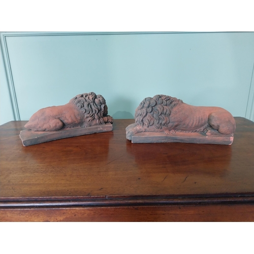 2121 - Pair of moulded terracotta statuettes of recumbent lions {13 cm H x 30 cm W x 11 cm D}.