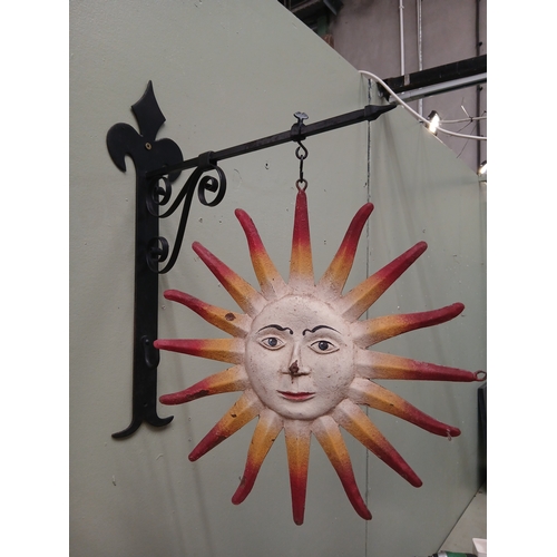 46 - Metal sun trade sign with hand painted face and radiating rays, hanging from decorative metal bracke... 