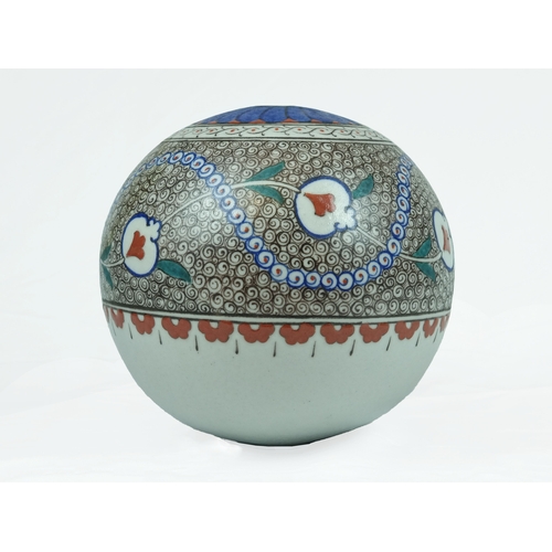 A Kutahya Ornamental Pottery Ball, Ottoman Turkey, 20th Century. 

Of bulbous form decorated with scrolling stylised pomegranates and leaves intersecting with spiralling cobalt-blue and red motifs amidst wave and rock design, surmounted by a band of scrolling motifs, the top is pierced and decorated with cobalt-blue petals, 18cm diameter, 18.5cm high