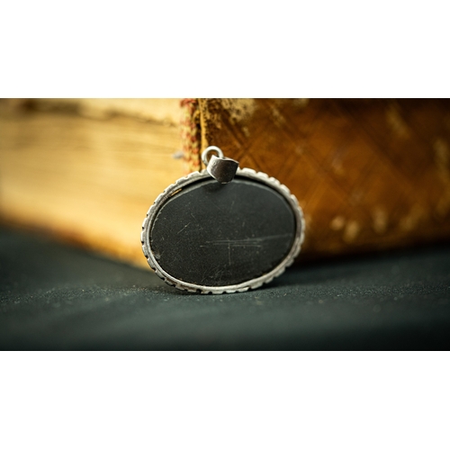 27 - A SILVER FRAMED DARK HARD STONE PENDANT Of oval form, the surface engraved with Persian nasta’liq in... 