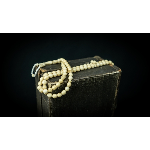 54 - A MORS TOOTH PRAYER BEADS, The tasbih strung  with 99 bone spherical  beads, flat stops, narrowing a... 