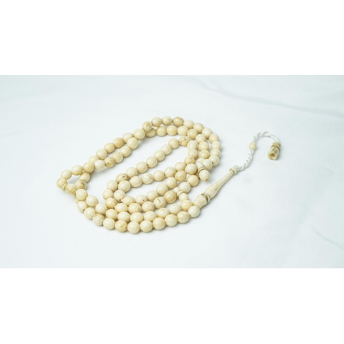 54 - A MORS TOOTH PRAYER BEADS, The tasbih strung  with 99 bone spherical  beads, flat stops, narrowing a... 