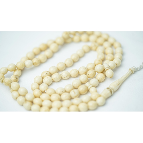 54 - A MORS TOOTH PRAYER BEADS, The tasbih strung  with 99 bone spherical  beads, flat stops, narrowing a... 