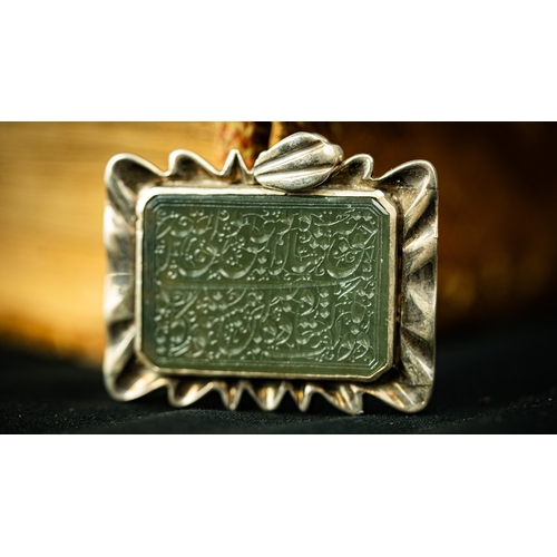 7 - A RECTANGULAR FORM SILVER FRAMED GREEN JADE PENDANT Of square form, the jade surface engraved with A... 