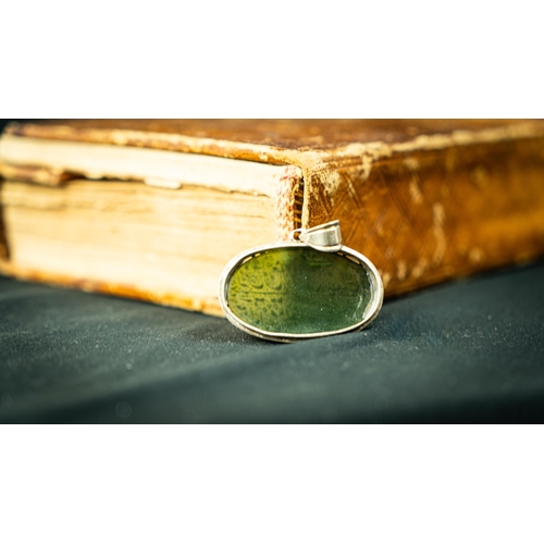 8 - AN OVAL FORM SILVER FRAMED GREEN JADE PENDANT Of oval form, two lines of Arabic inscription engraved... 